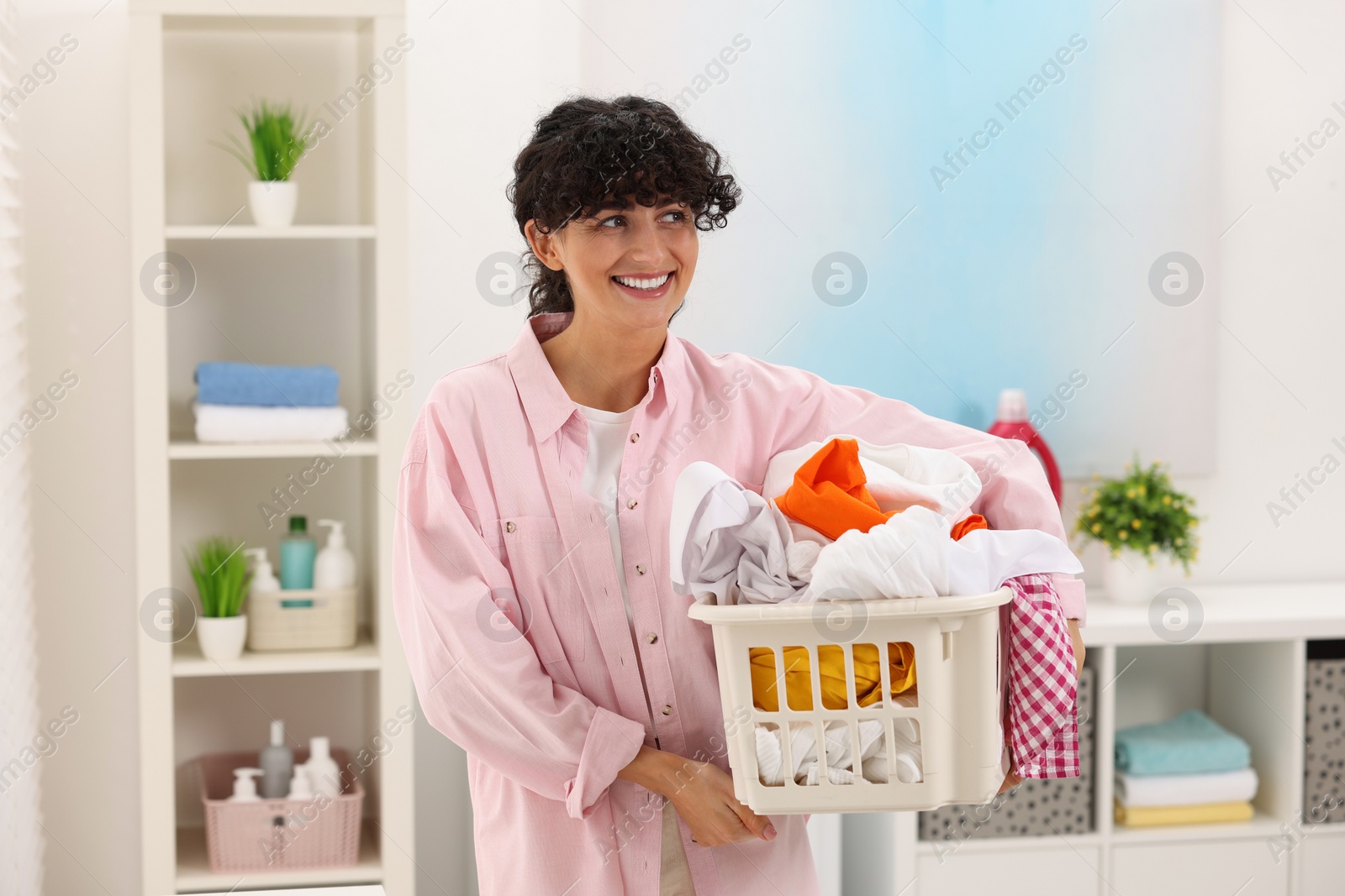 Photo of Happy woman with laundry basket full of clothes indoors