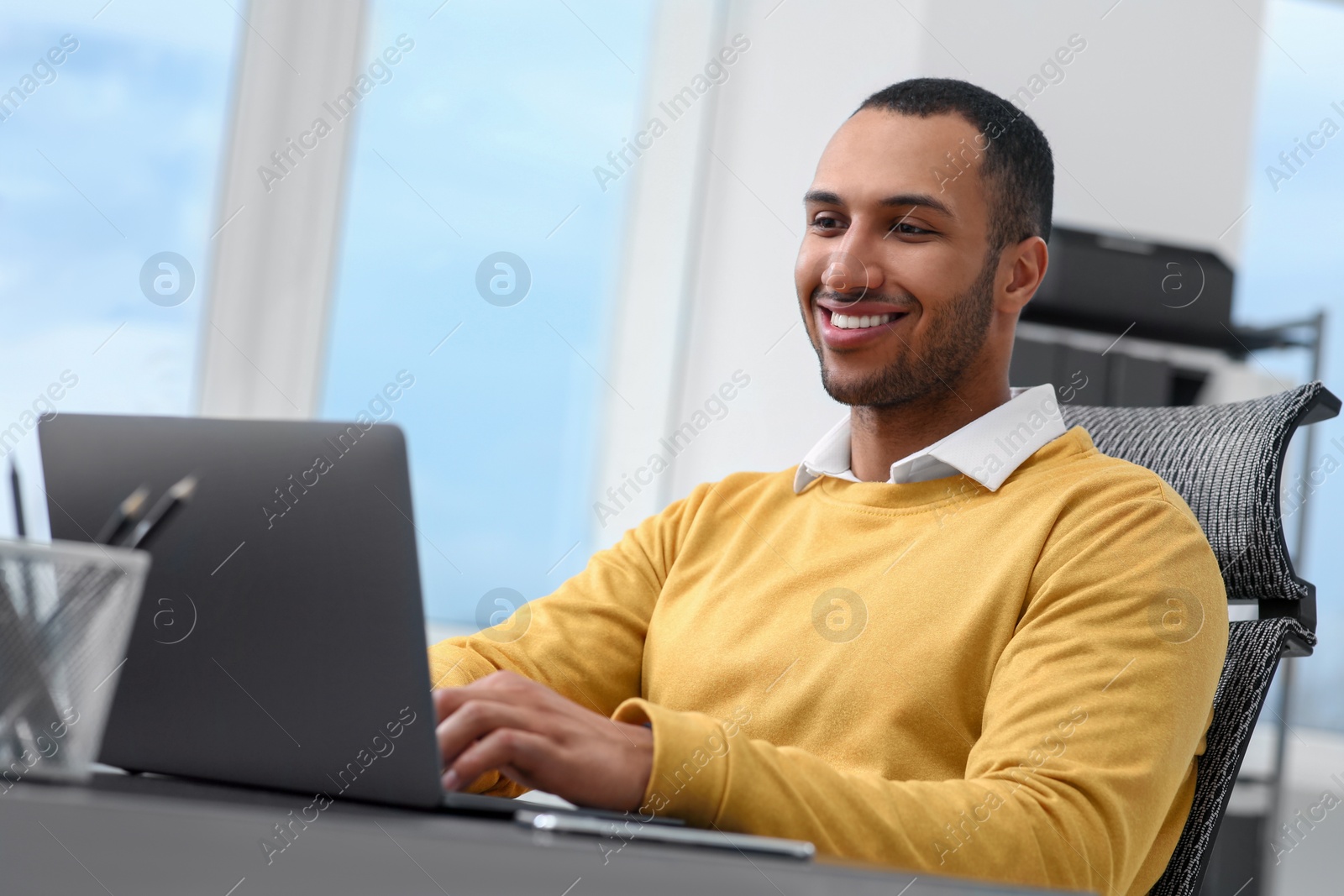 Photo of Young man working on laptop at table in office