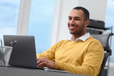 Photo of Young man working on laptop at table in office