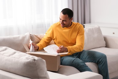 Photo of Happy young man opening parcel at home. Internet shopping