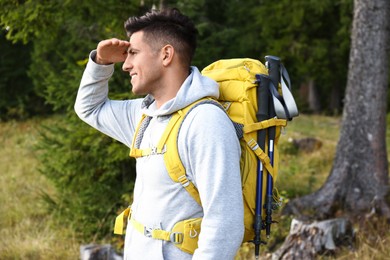 Man with backpack and trekking poles hiking in forest