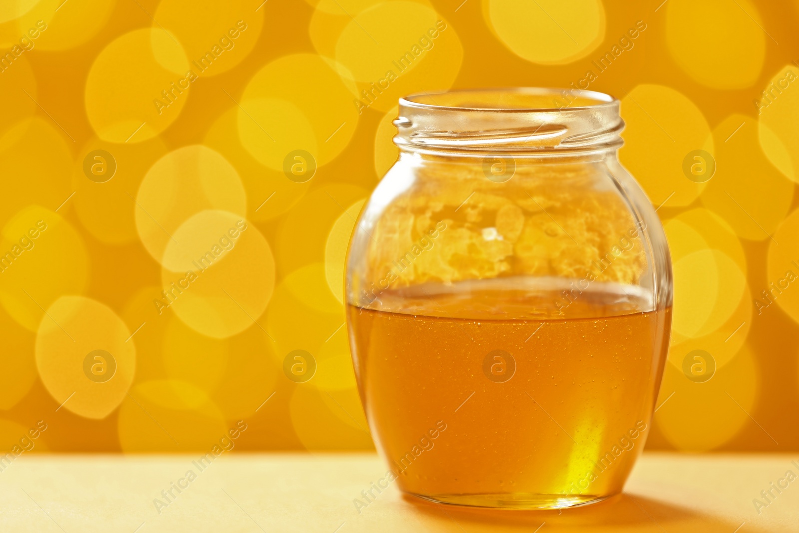 Photo of Jar with fresh honey on table against blurred background. Space for text