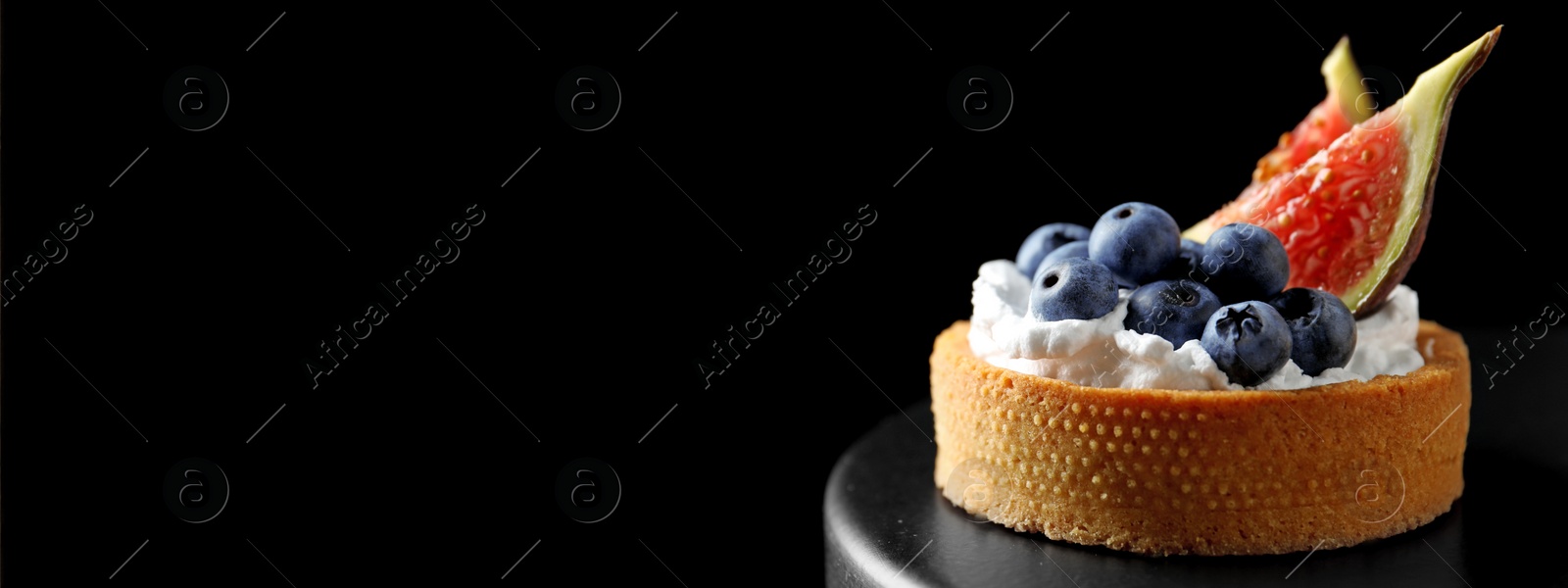 Image of Delicious tartlet with fresh blueberries and figs on cake stand against black background, space for text. Banner design