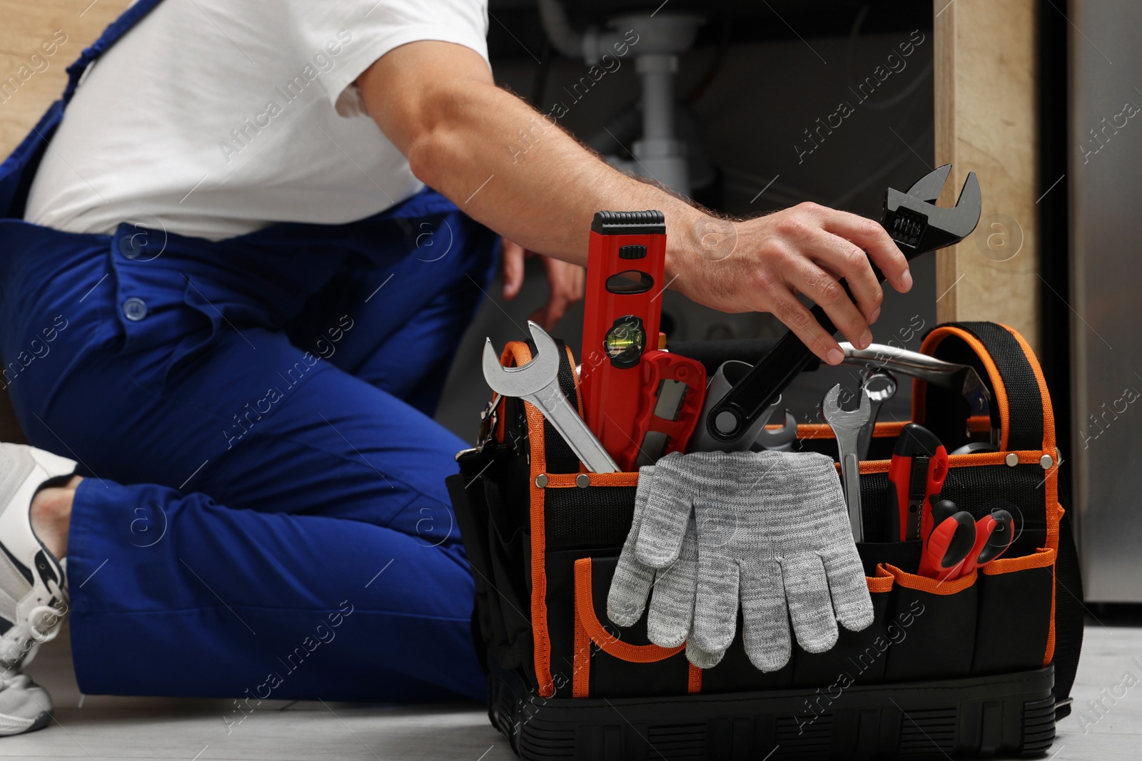 Photo of Professional plumber taking adjustable wrench from tool bag indoors, closeup