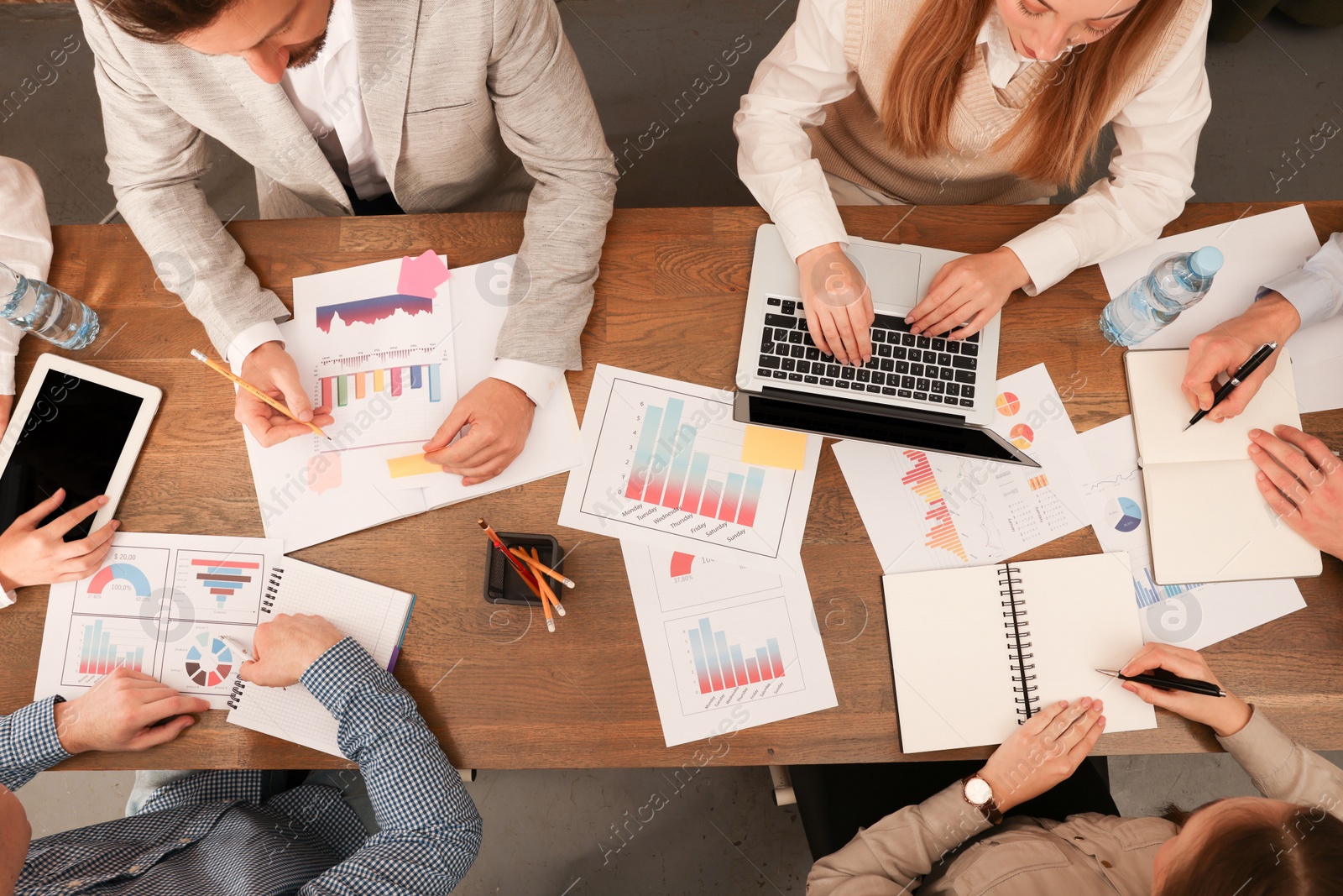 Photo of Team of employees working together at wooden table in office, above view