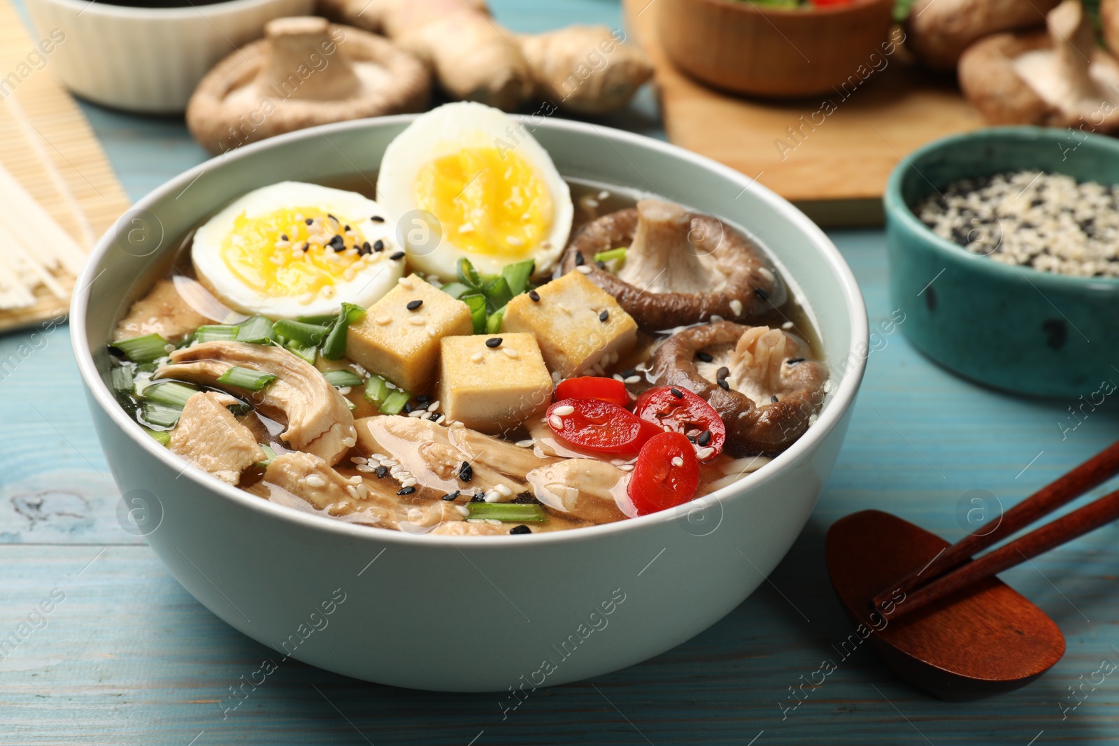 Photo of Bowl of delicious ramen and ingredients on light blue wooden table. Noodle soup