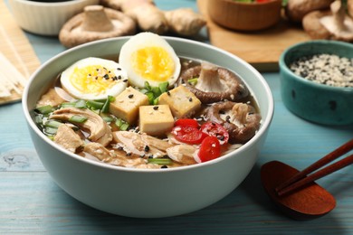 Photo of Bowl of delicious ramen and ingredients on light blue wooden table. Noodle soup