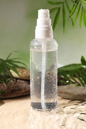 Photo of Wet bottle of micellar water, leaves and spa stones against green background