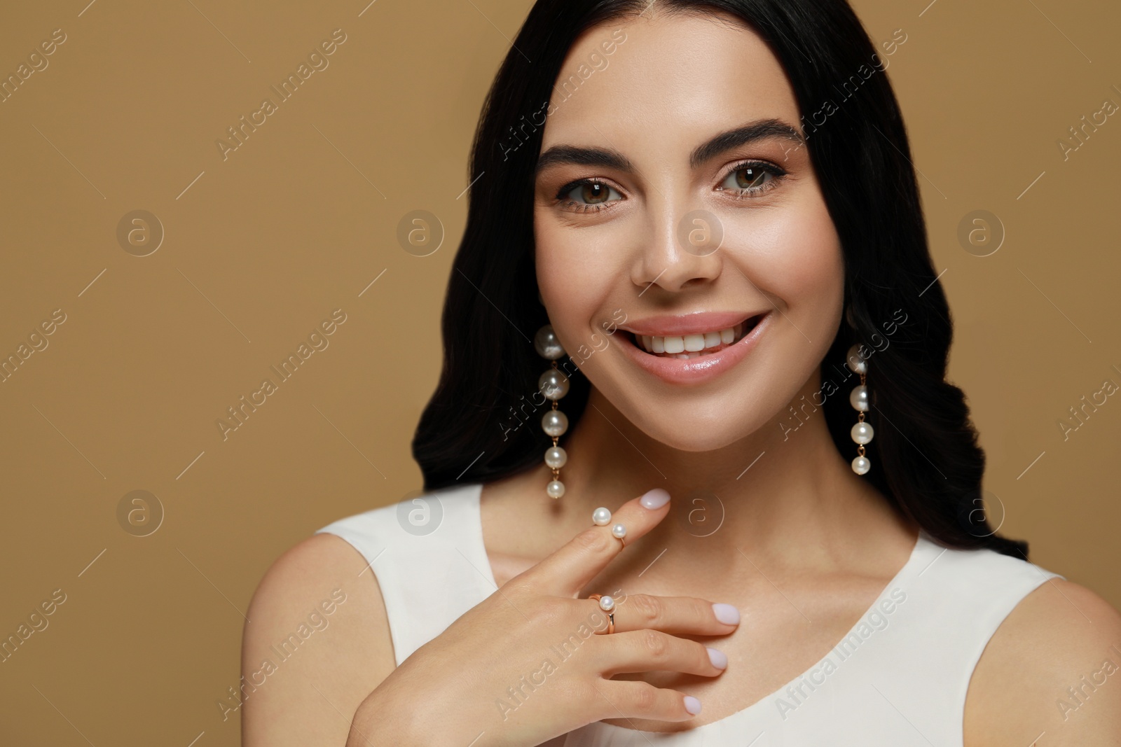 Photo of Young woman wearing elegant pearl jewelry on brown background, space for text