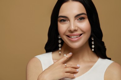 Young woman wearing elegant pearl jewelry on brown background, space for text