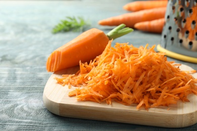 Photo of Board with grated carrot on wooden background, closeup