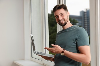 Handsome man with laptop near window indoors
