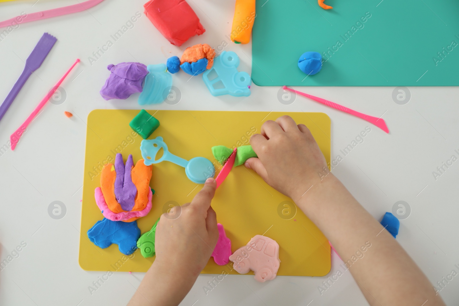 Photo of Little girl sculpting with play dough at white table, top view