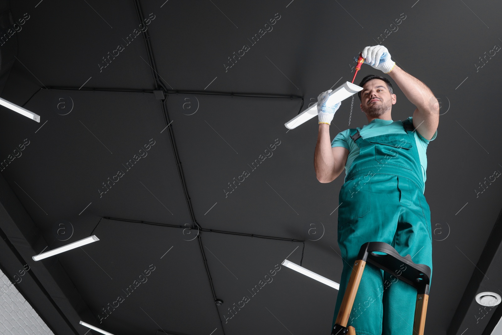 Photo of Ceiling light. Electrician installing led linear lamp indoors, low angle view. Space for text