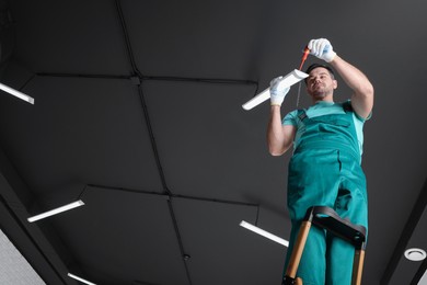 Ceiling light. Electrician installing led linear lamp indoors, low angle view. Space for text