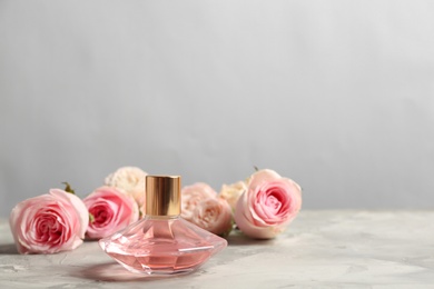 Bottle of perfume with beautiful roses on table, space for text