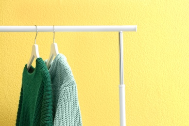 Photo of Warm sweaters hanging on rack near yellow wall, closeup