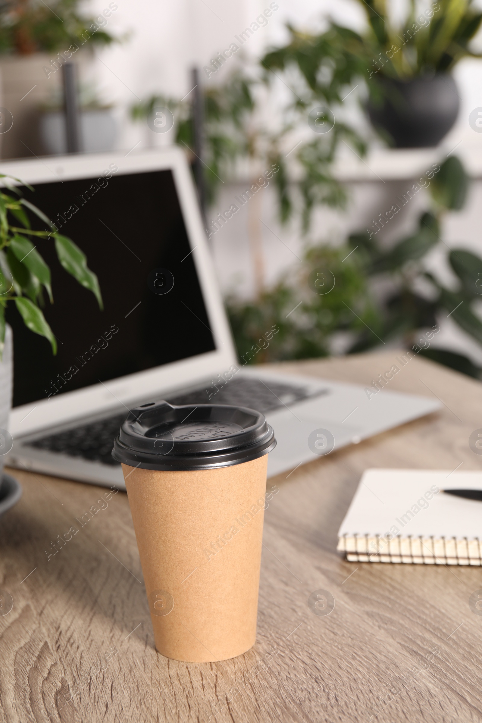 Photo of Paper cup, notebook and laptop on wooden table in room