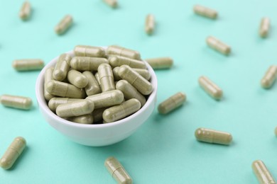 Bowl with vitamin capsules on turquoise background, closeup