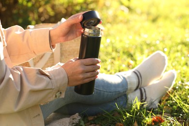 Woman opening thermos on green grass outdoors, closeup