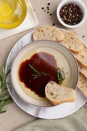 Photo of Bowl of balsamic vinegar with oil, rosemary, bread slices and spices on table, flat lay