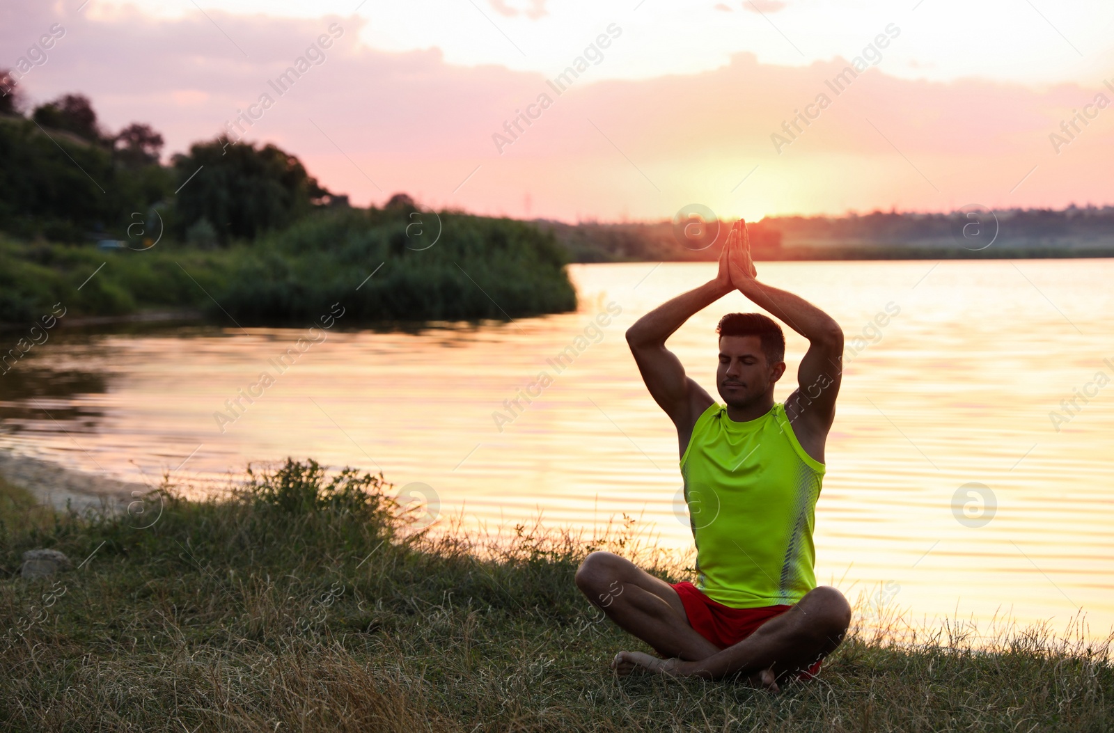 Photo of Man meditating near river at sunset. Space for text