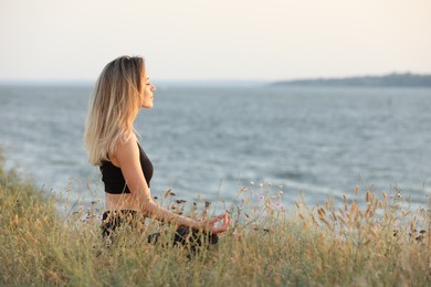 Young woman meditating near river on sunny day, space for text