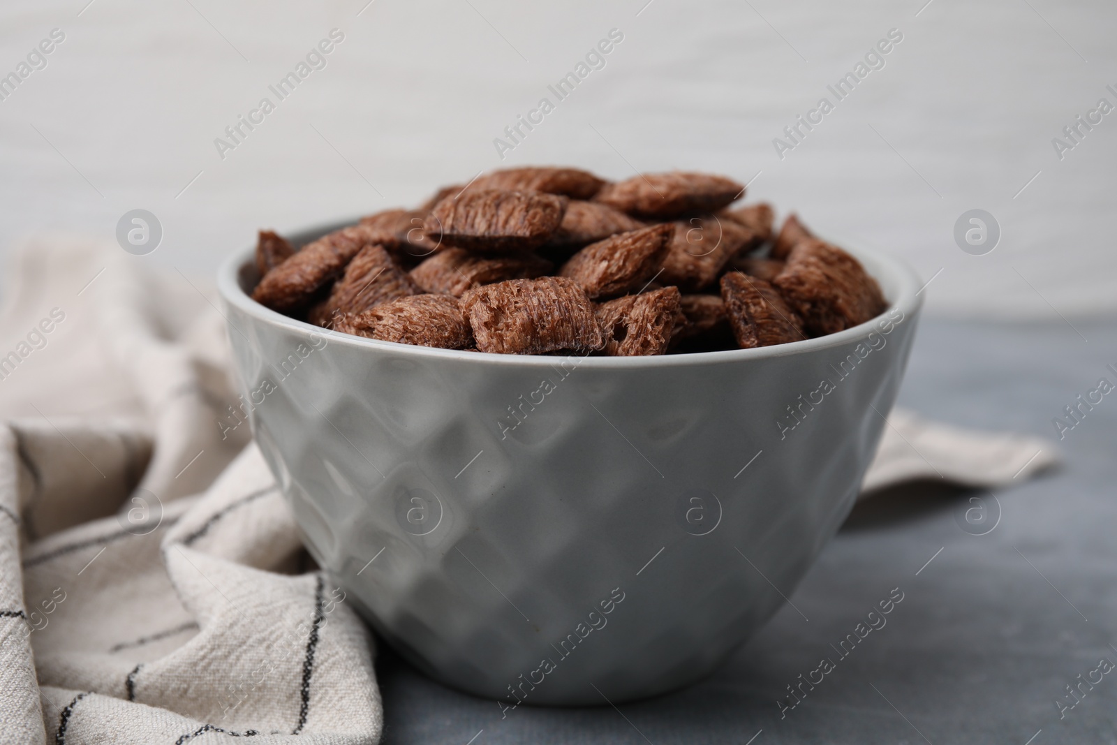 Photo of Chocolate cereal pads in bowl on grey table, closeup