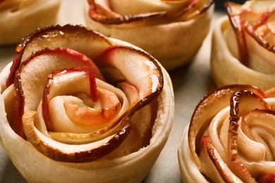 Photo of Freshly baked apple roses on parchment paper, closeup. Beautiful dessert