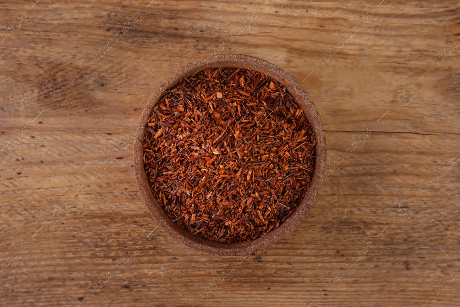 Photo of Dry rooibos leaves in bowl on wooden table, top view