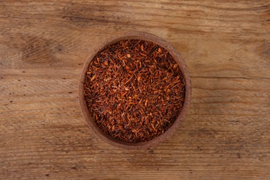 Dry rooibos leaves in bowl on wooden table, top view