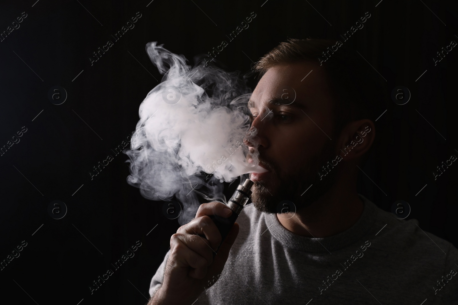 Photo of Man using electronic cigarette on black background