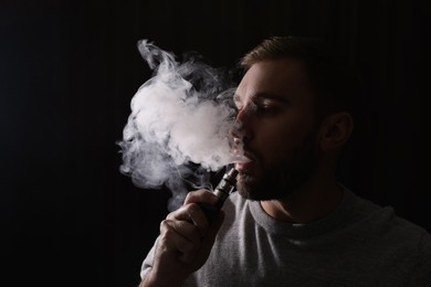 Photo of Man using electronic cigarette on black background