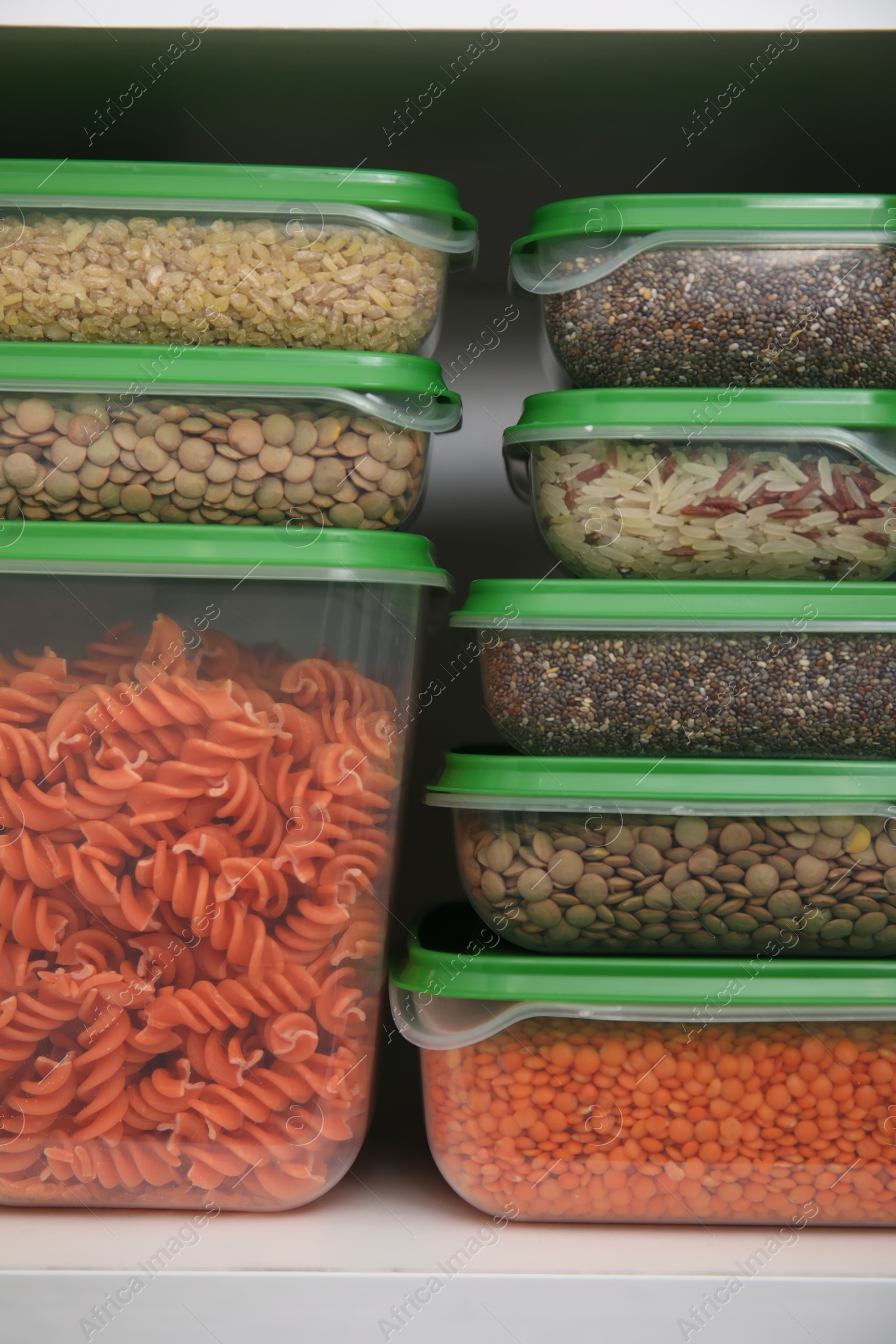 Photo of Plastic containers filled with food products in kitchen cabinet, closeup