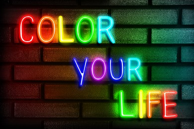 Glowing neon sign with phrase Color Your Life on brick wall