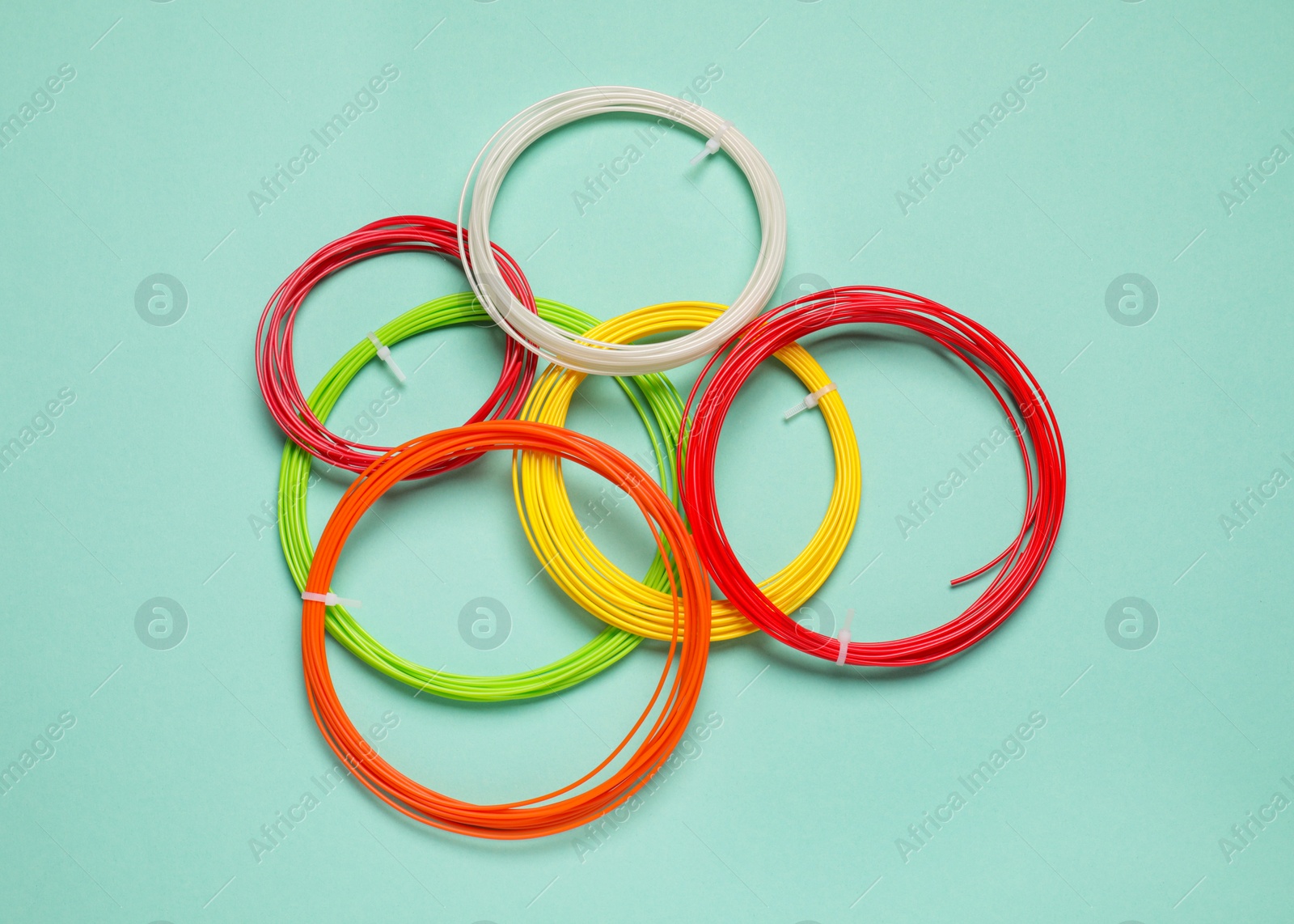 Photo of Colorful plastic filaments for 3D pen on turquoise background, flat lay