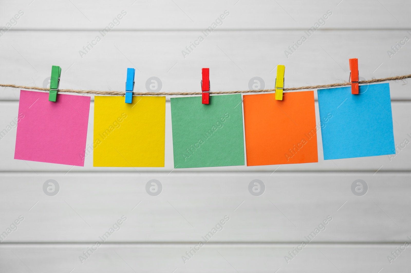 Photo of Clothespins with colorful blank notepapers on twine against white wooden background. Space for text