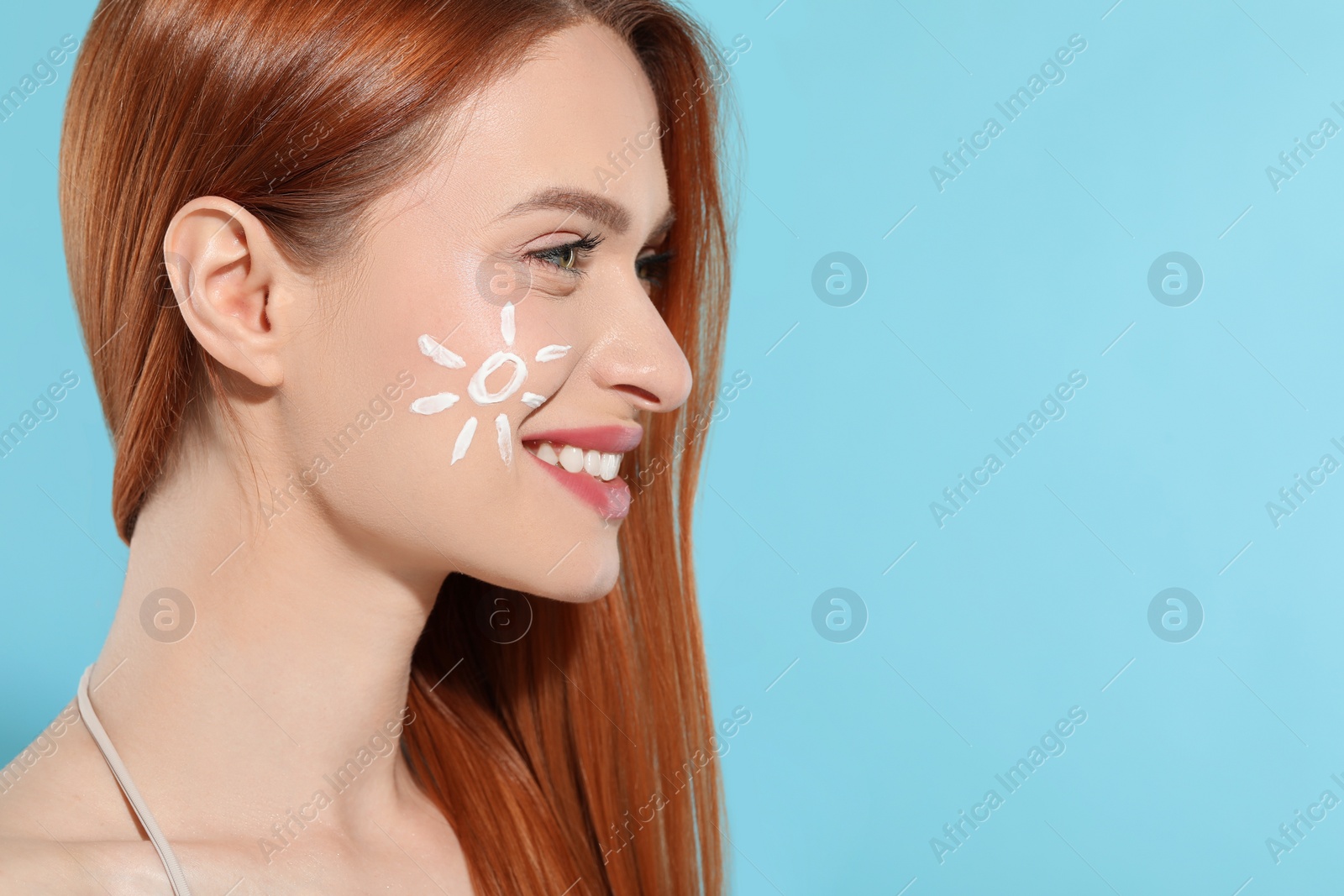 Photo of Beautiful young woman with sun protection cream on her face against light blue background, space for text