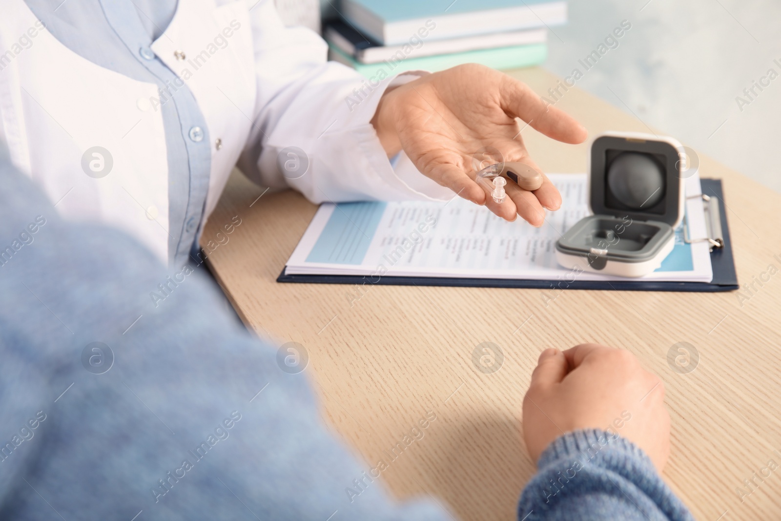 Photo of Doctor giving patient hearing aid at table in clinic, closeup