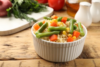 Photo of Delicious bulgur with vegetables on wooden table, closeup