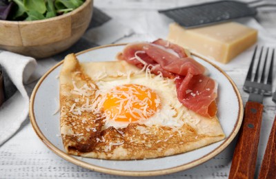 Delicious crepe with egg served on white wooden table, closeup. Breton galette