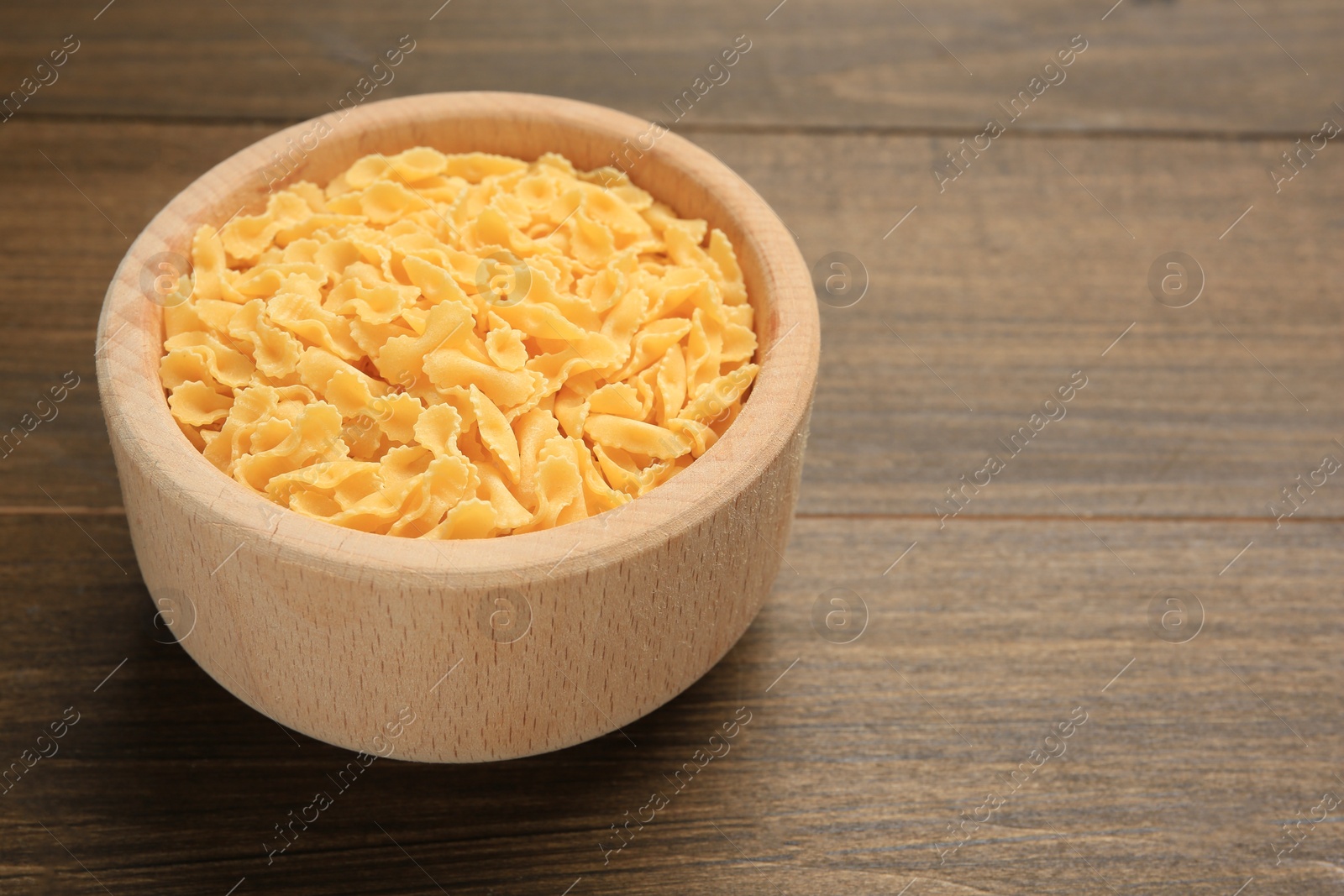 Photo of Raw farfalline pasta in bowl on wooden table, closeup. Space for text