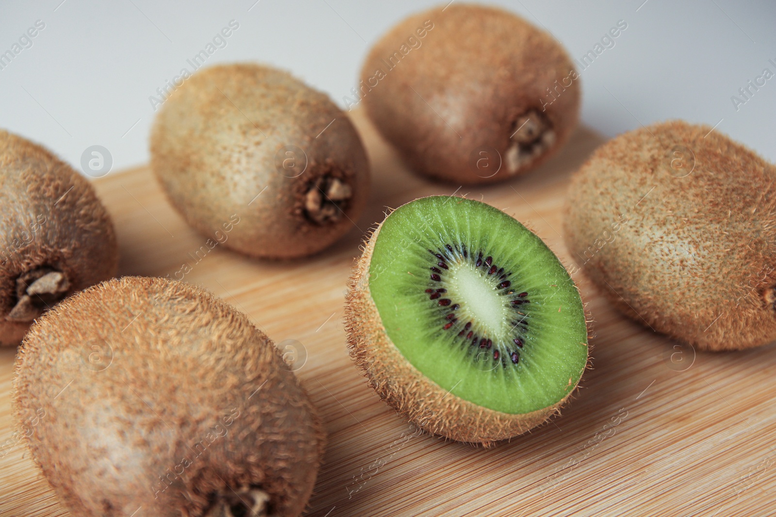 Photo of Wooden board with whole kiwis and cut one on beige background, closeup
