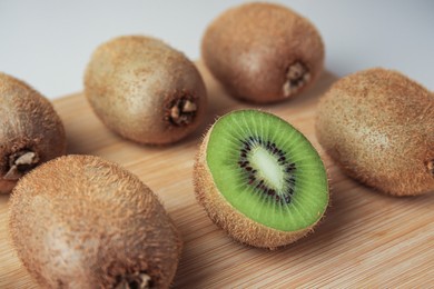 Photo of Wooden board with whole kiwis and cut one on beige background, closeup