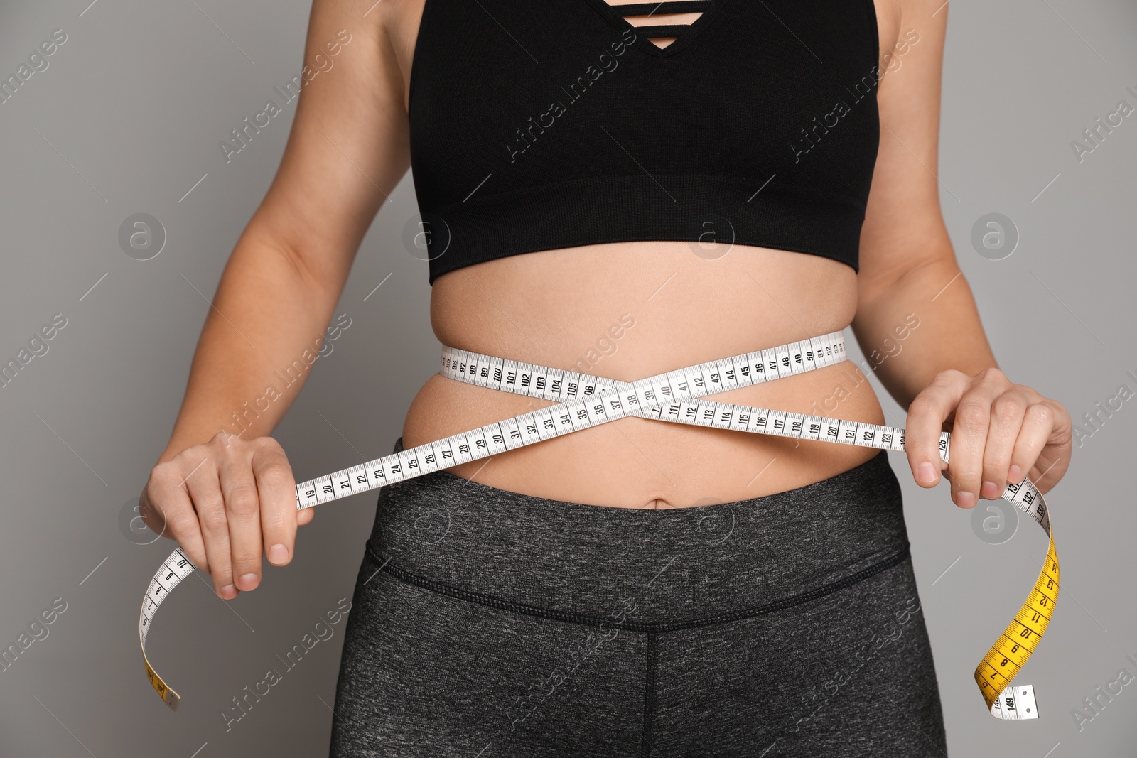 Photo of Woman measuring waist with tape on grey background, closeup