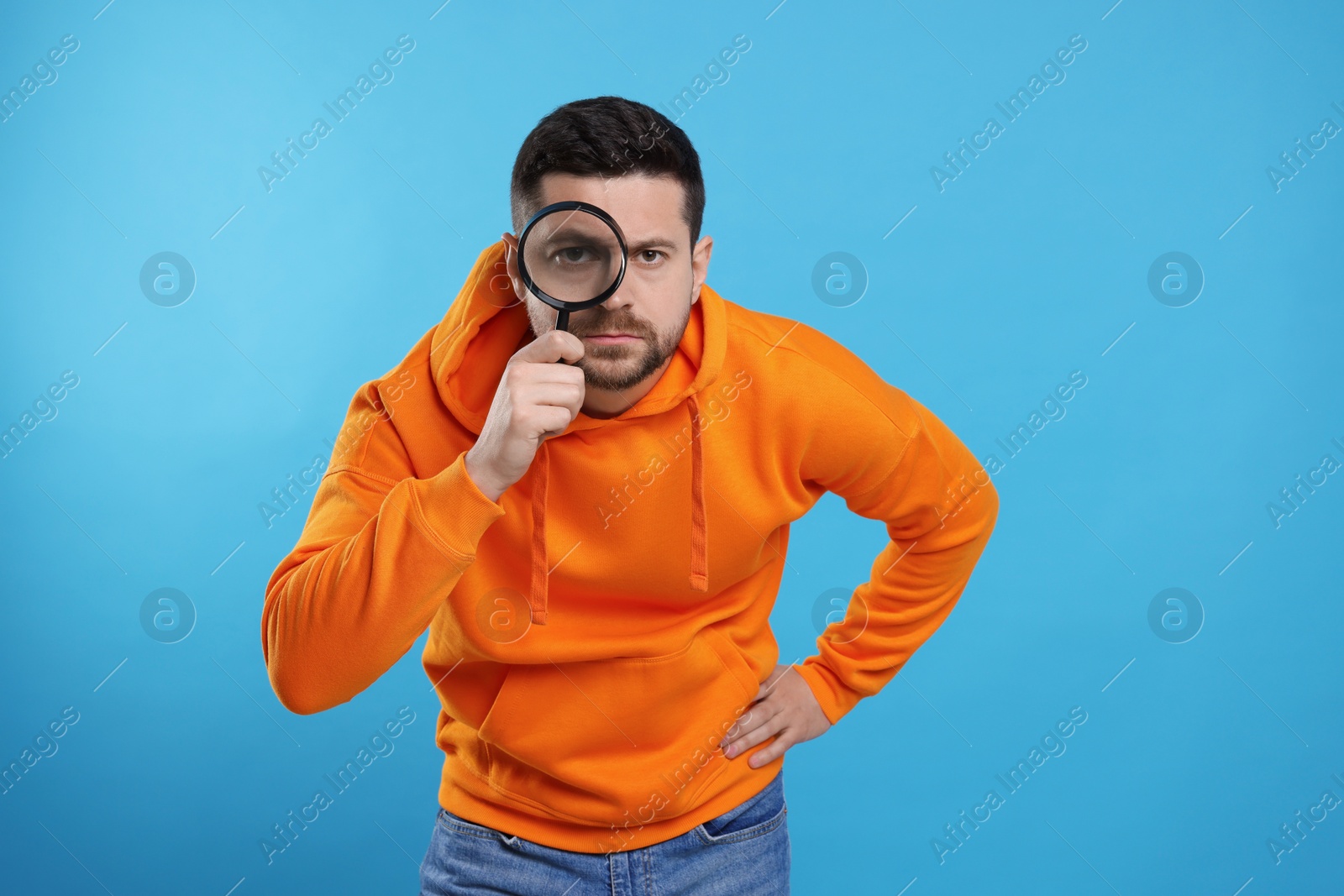 Photo of Man looking through magnifier glass on light blue background