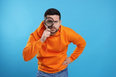 Photo of Man looking through magnifier glass on light blue background