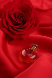 Photo of Heart shaped bottle of love potion and rose flower on red fabric