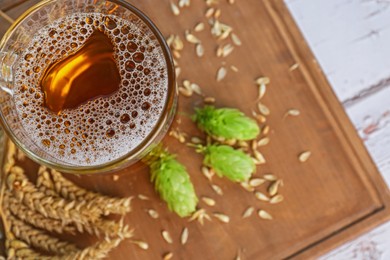 Photo of Mug with beer, fresh hops and ears of wheat on white wooden table, top view. Space for text