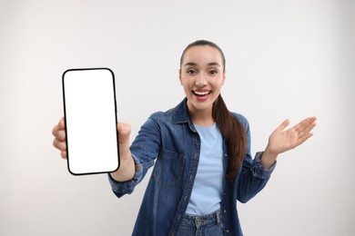 Photo of Surprised young woman showing smartphone in hand on white background